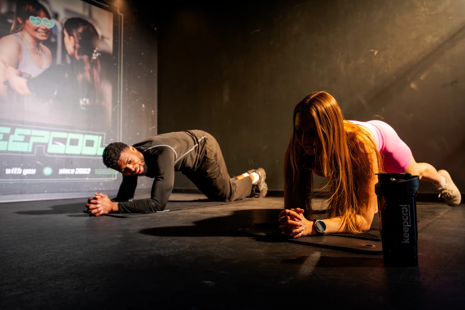 Deux athlètes en position de gainage sur scène, exercice abdominaux intensif, salle de sport Keepcool.