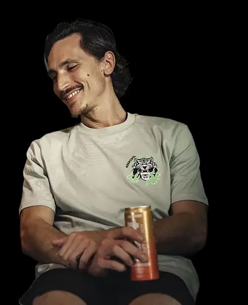 Homme souriant assis, tenant une canette orange avec un t-shirt beige à motif tigre vert.